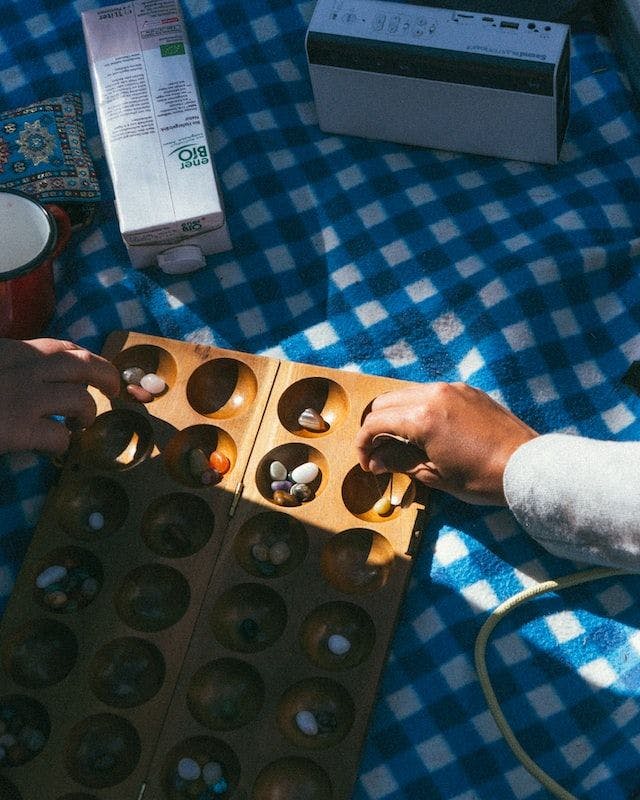 Two people playing mancala game on a picnic blanket